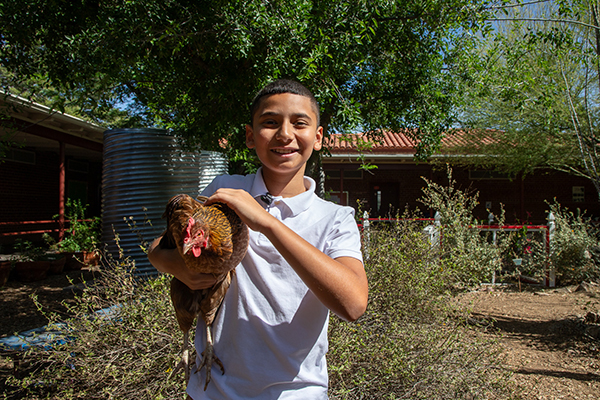 A boy smiles as he holds one of the school's chickens