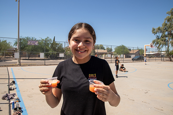 A girl smiles as she holds up two small smoothie cups