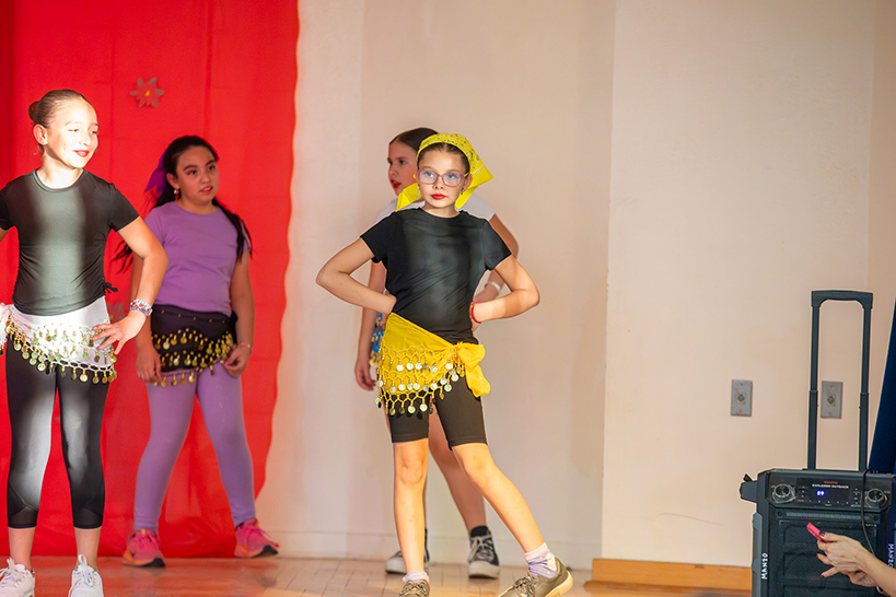 Girls wearing colorful coin skirts dance on stage