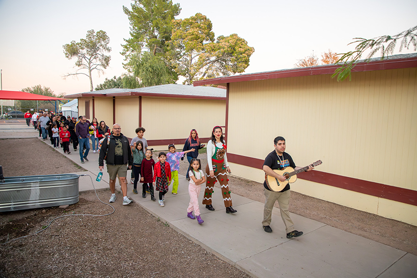 A man playing guitar leads families in a procession around the school