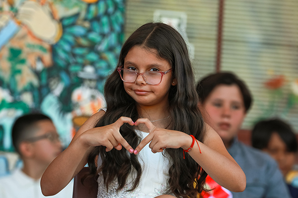 A little girl wearing glasses makes a heart shape with her fingers
