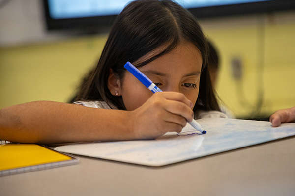 A girl writes on a whiteboard at her desk