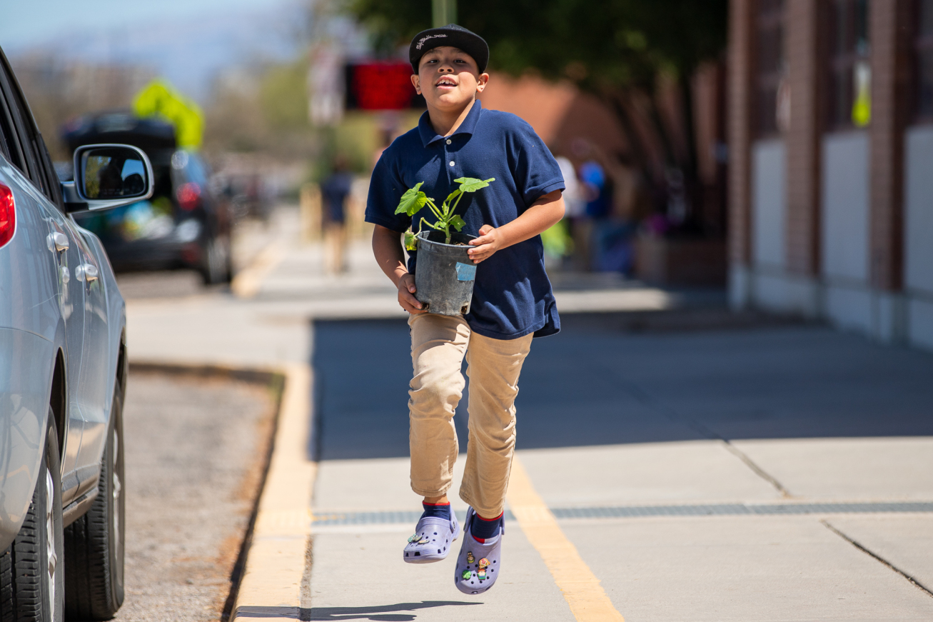 A boy runs down the sidewalk holding a potted plant